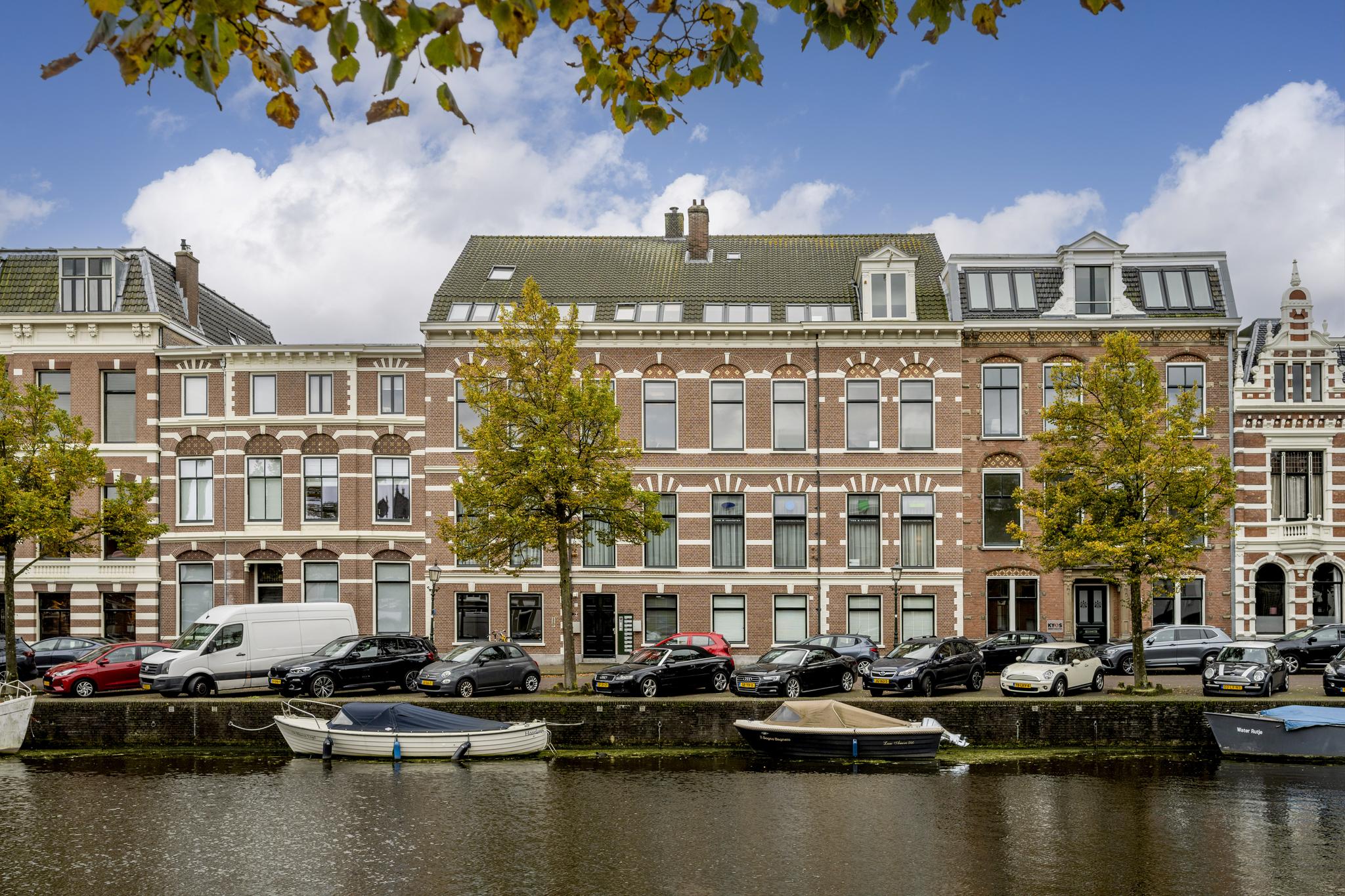 Rij monumentale herenhuizen aan de Nieuwe Gracht in Utrecht, met geparkeerde auto's en boten langs het water.